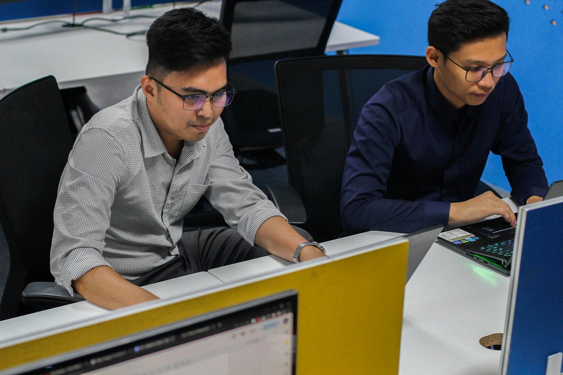  Two Asian men seated at computers, focused on their monitors while engaged in study.