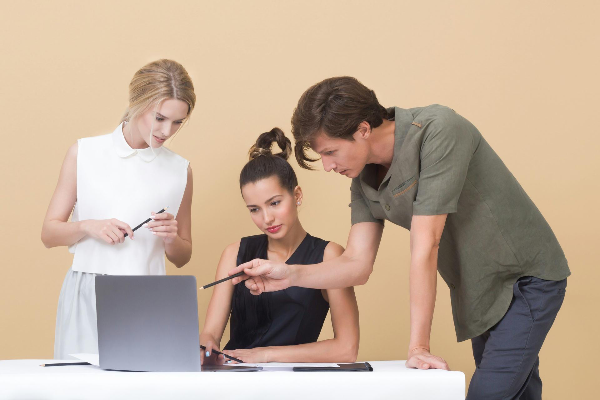 Three individuals collaborate on a laptop, focused on their work together.