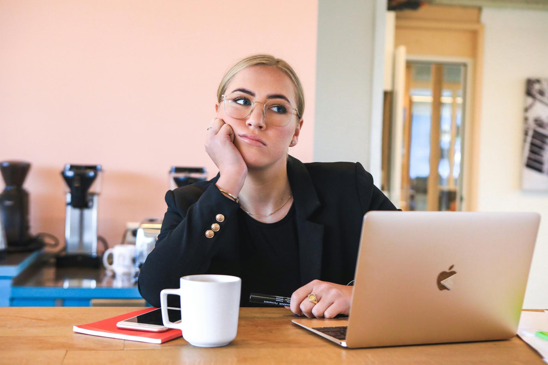  A woman at a table, focused on her laptop with a steaming cup of coffee beside her.